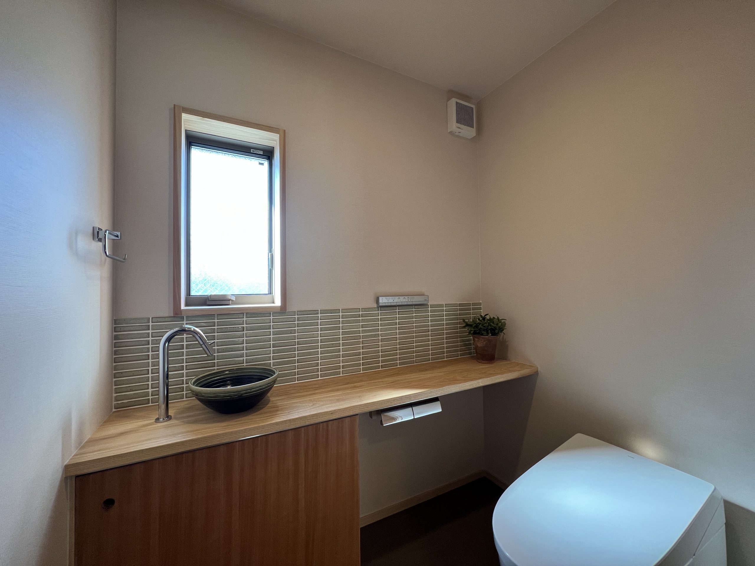 造作収納を設けたトイレはタイルや手洗い器を緑で統一したシンプルな造りに。